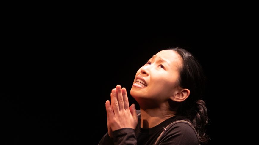 Actor Zoe Kim sits on the floor, palms in prayer, looking up. 