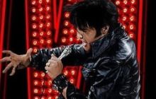 Image of Elvis in black leather outfit with Elvis sign in red lights behind