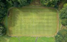 A bird's eye view of a grass, football pitch surrounded by lush woodland