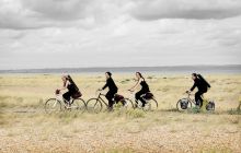 Four musicians ride through a field with instruments on their backs