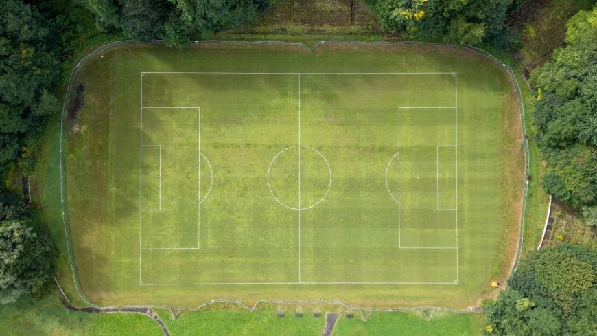 A bird's eye view of a grass, football pitch surrounded by lush woodland