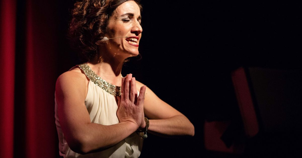Michaela Burger wearing a white outfit with silver sequins, hands clasped, mid-song