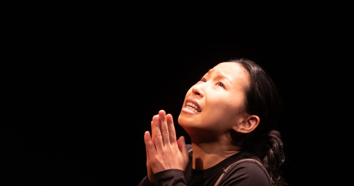 Actor Zoe Kim sits on the floor, palms in prayer, looking up. 