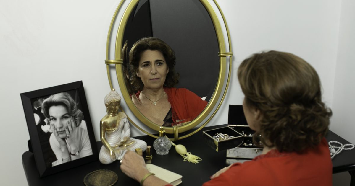 Performer Karin Trachtenberg poses in front of a mirror, a photo of her mother to the side.