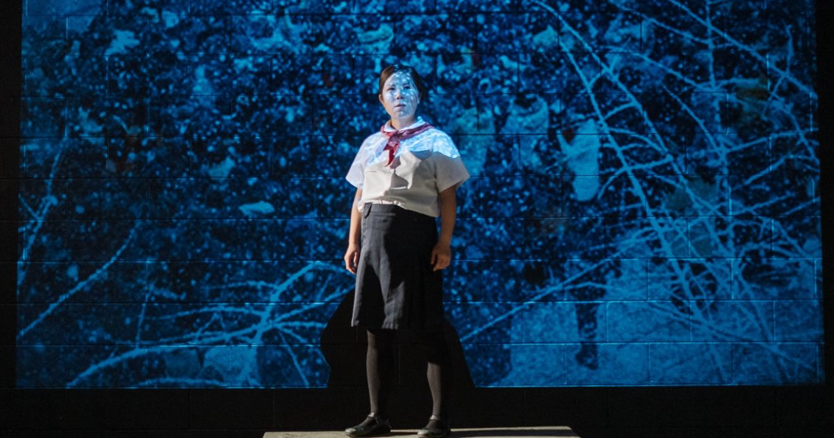 Sora Baek, standing in front of a map, arms stretched out, lit in blue light