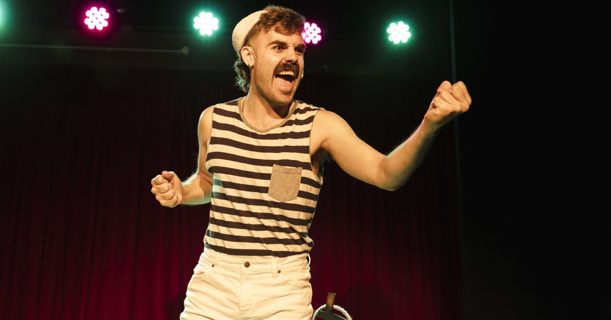 A performer stands in the middle of the frame, surrounded by light in the background.