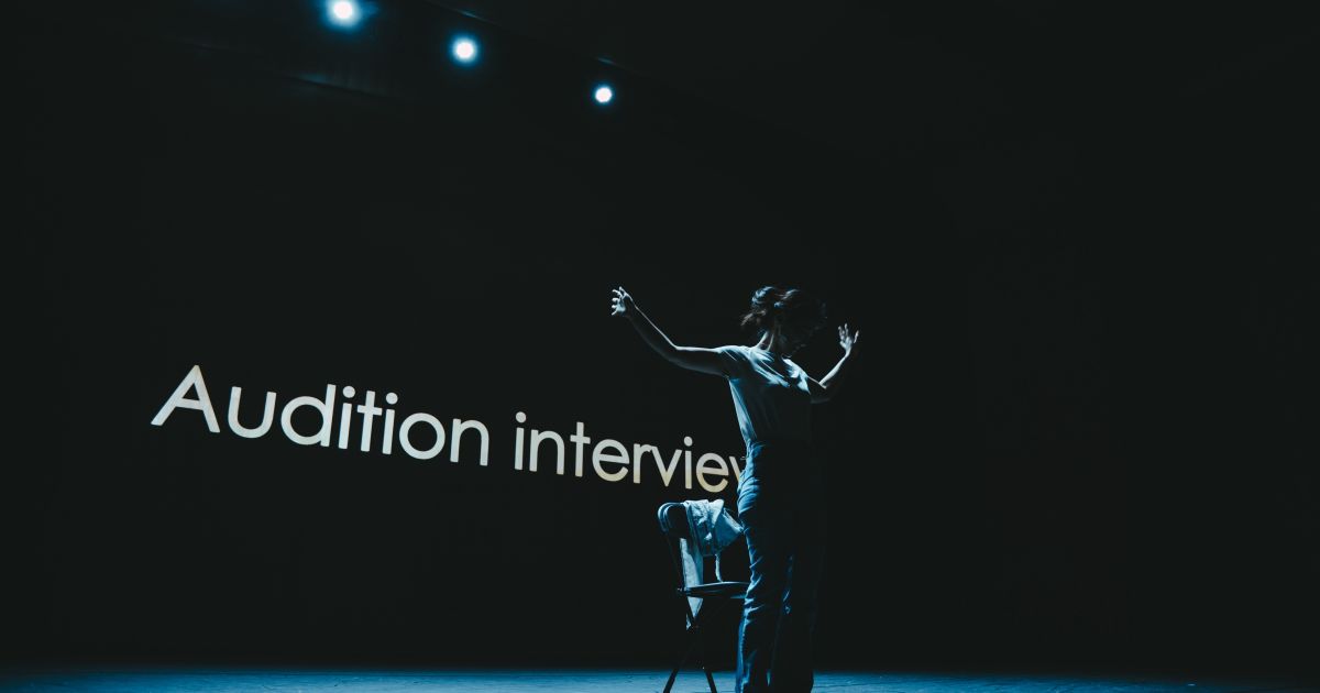 Hyojin Park stands in front of a screen on which the words 'Audition Interview' appear. The background is dark with the performer standing with arms outstretched in silhouette.