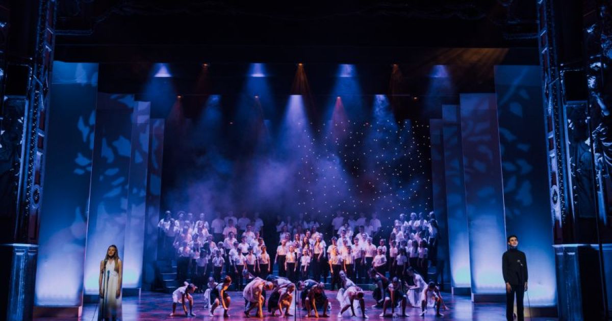 Soloists stand at either side of the stage, singing Falling Softly from Once. Dancers move in pair in the centre, beautifully covered in blue light.