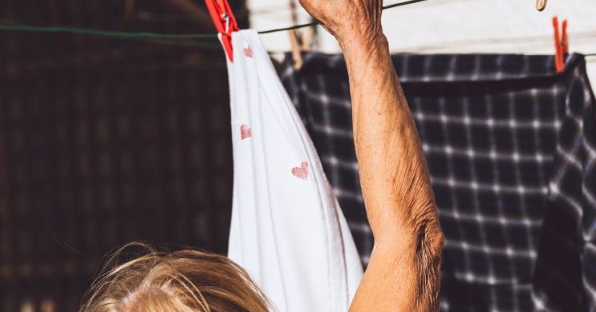 The arm and head of an older woman are shown, hanging out washing on a clothes line.