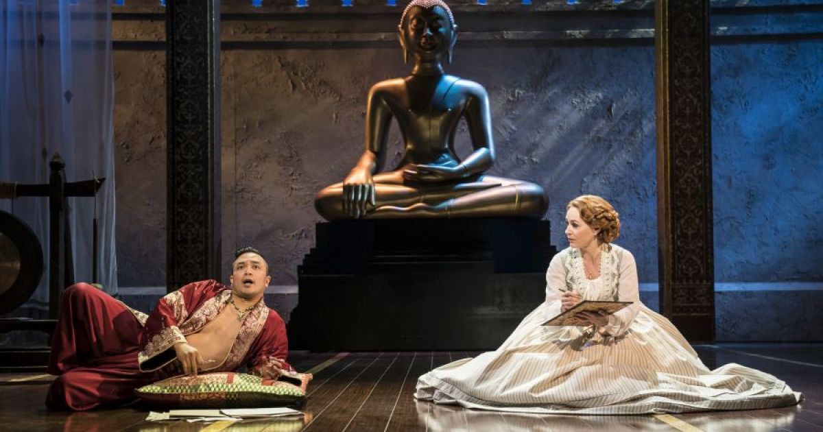 The King and Anna discuss a letter, the King propped up on an elbow and Anna seated on the floor in the King's chambers in front of a large statue of Budda. 